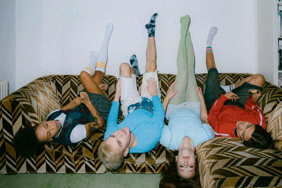 Group of four friends lying upside down on brown sofa vaping 