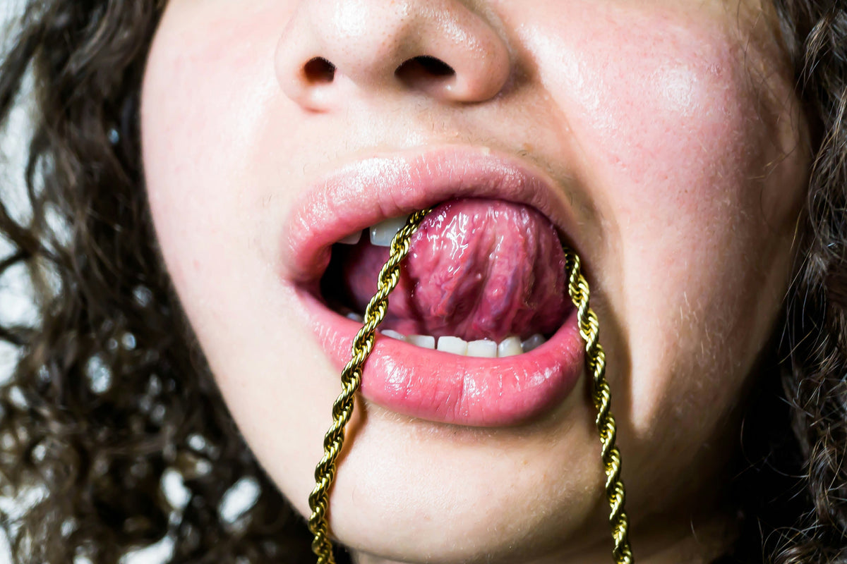 Person holding a gold chain between their lips, a common sign of oral fixation